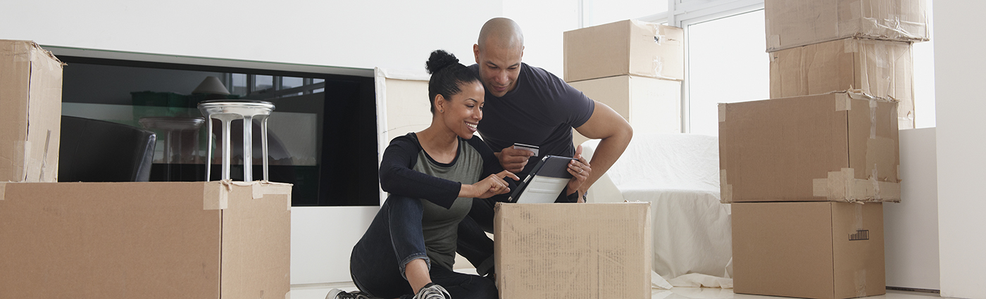 A man and woman sitting next to cardboard boxes and looking at a tablet device.